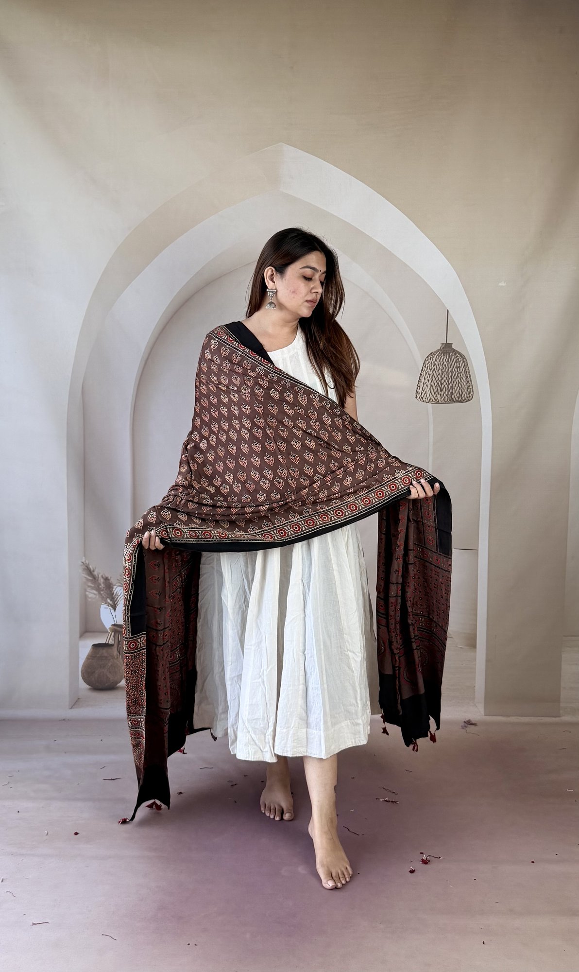 brown-ajrakh-modal silk-dupatta-paisley-buti-2 Brown Ajrakh modal silk dupatta draped over both arms showing paisley arch palla and tassels