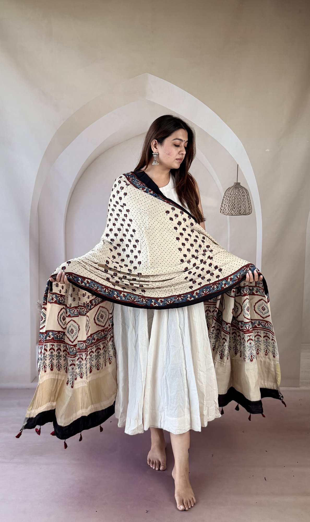 cream-ajrakh-modal silk-dupatta-buti-diamond-palla-2 Cream Ajrakh modal silk dupatta draped over both arms showing diamond medallion palla and tassels